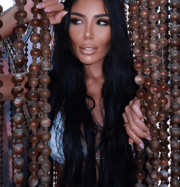 Eine Frau mit langen, schwarzen Haaren steht hinter einer dekorativen Perlenvorhang und blickt nachdenklich zur Seite.